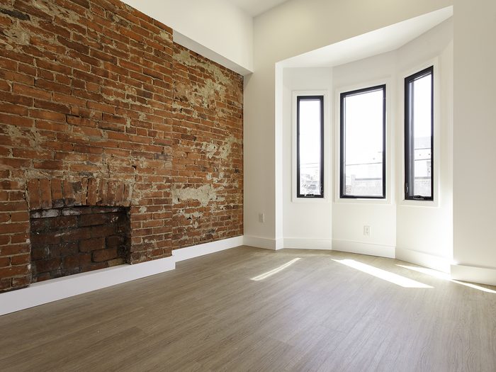 Empty room with an exposed brick wall, an old fireplace and a bay window