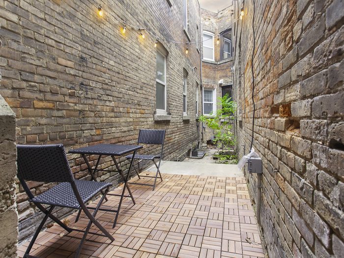 Brick-walled courtyard with a small table, two chairs and string lights