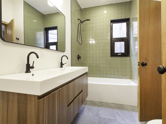 Bathroom with green tile, a wooden double vanity and black fixtures