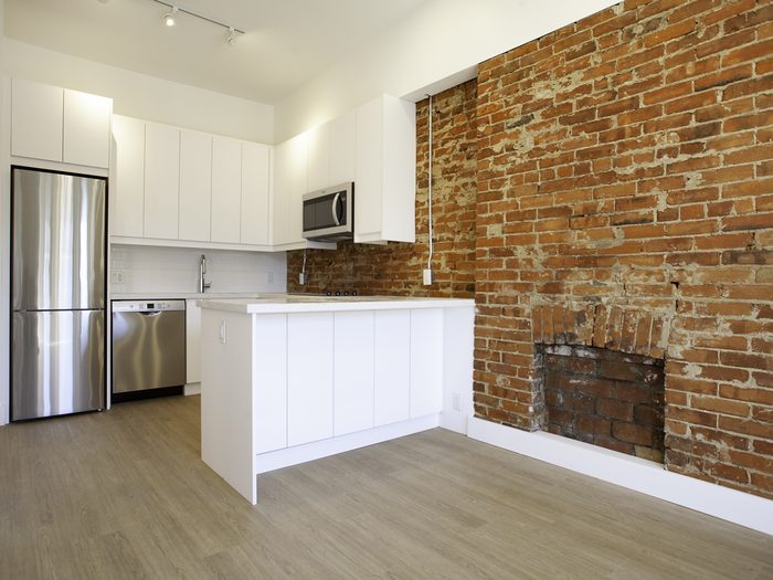 Kitchen with white cabinets beside an exposed brick wall and an old fireplace